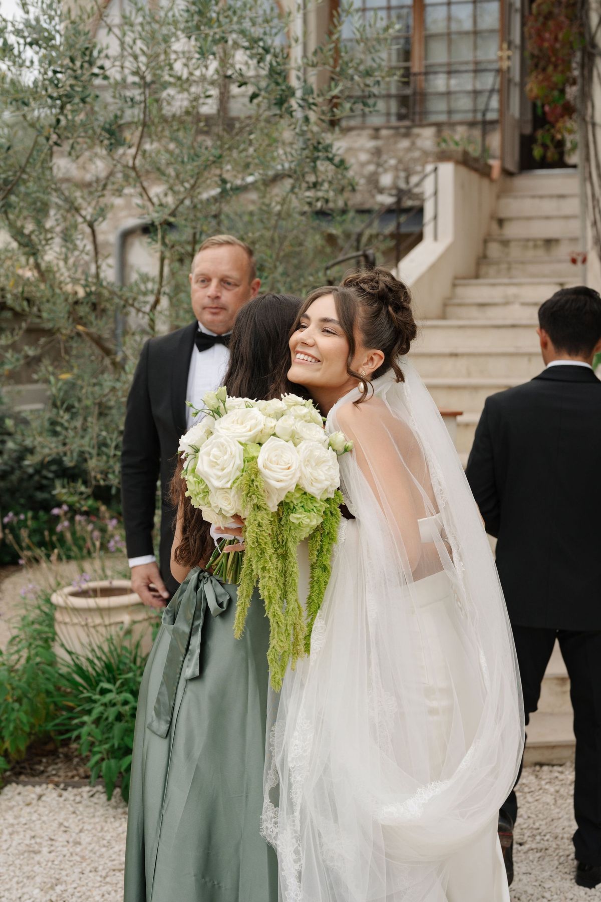 Bride hugging guest while holding bouquet after outdoor ceremony