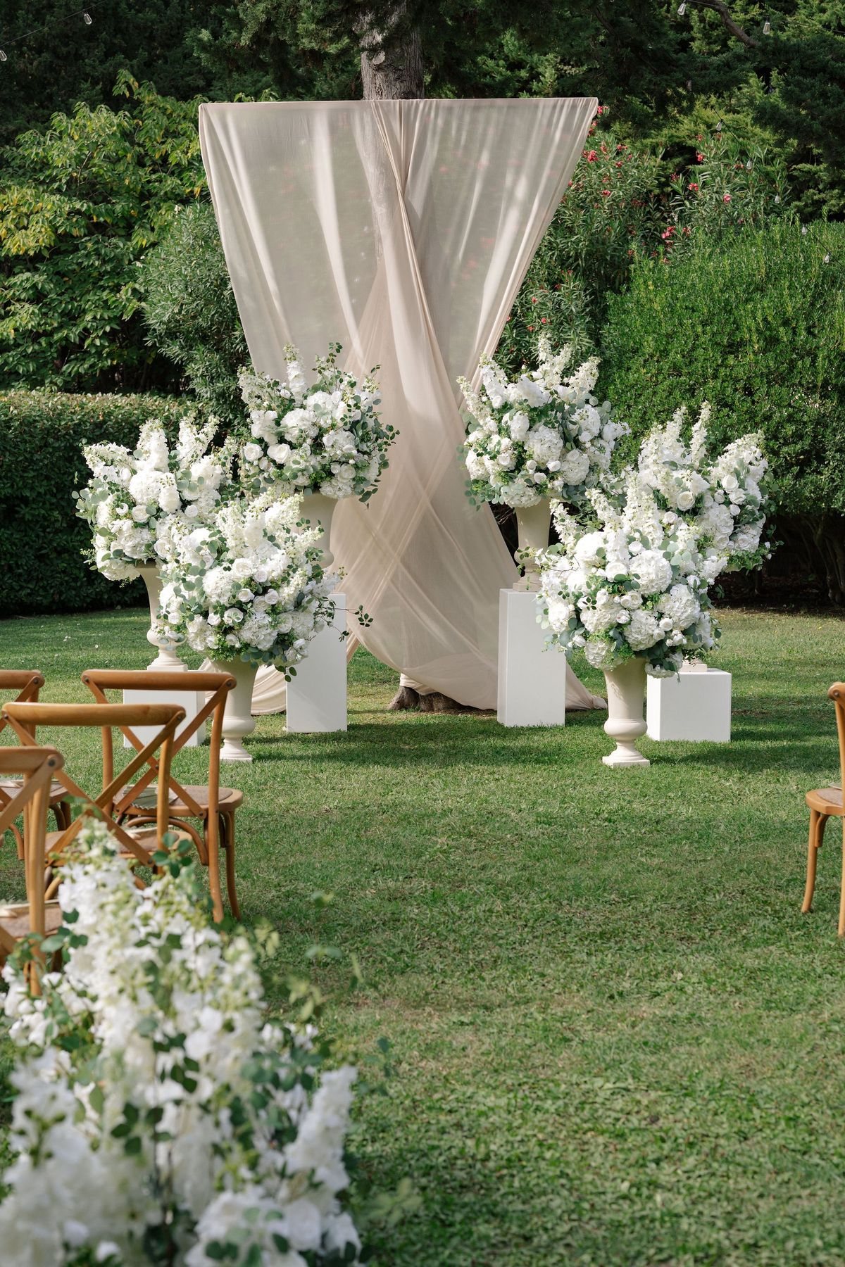 Outdoor ceremony altar with draped fabric and tall white floral urns