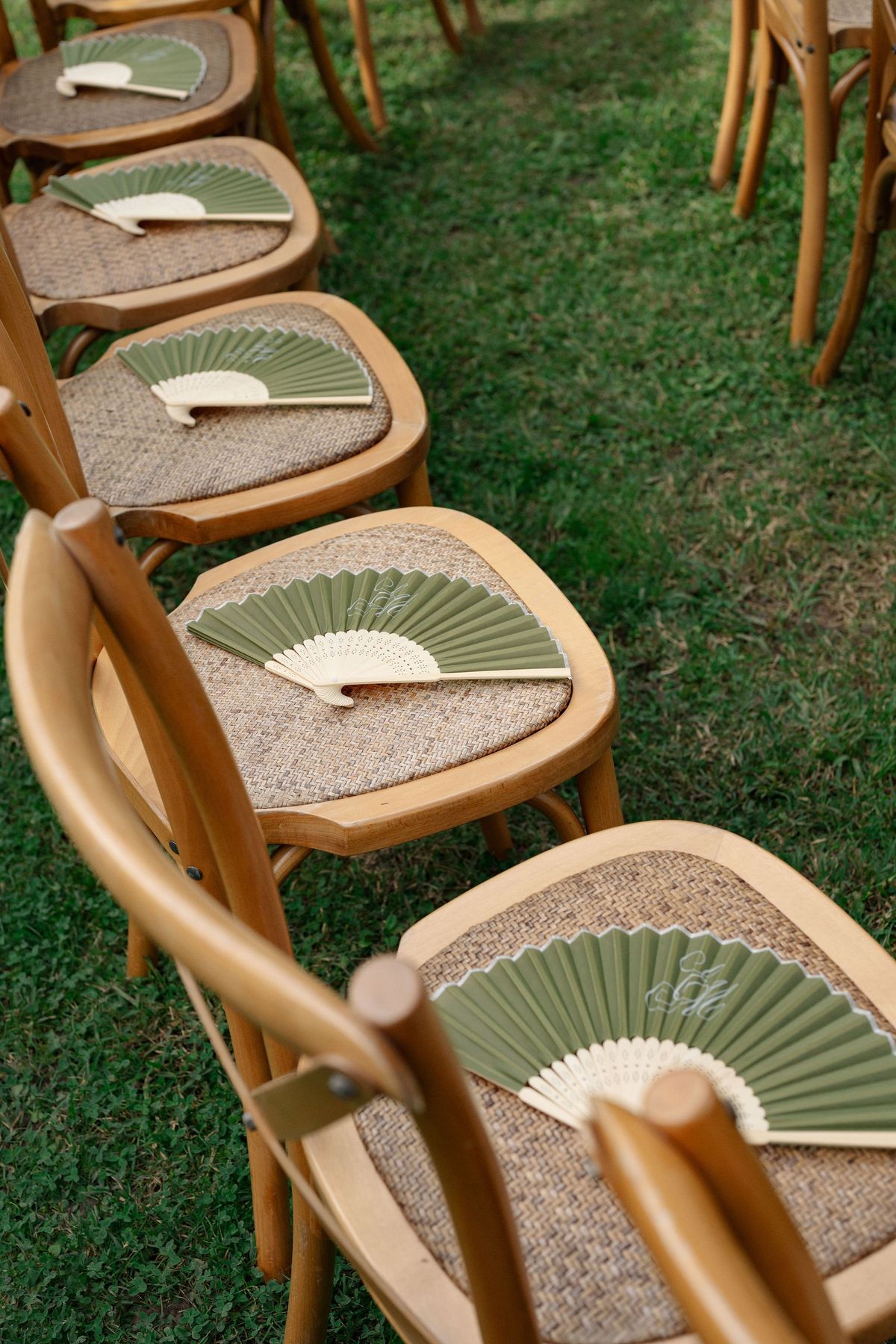 Row of wooden ceremony chairs with sage paper fan favours on seats
