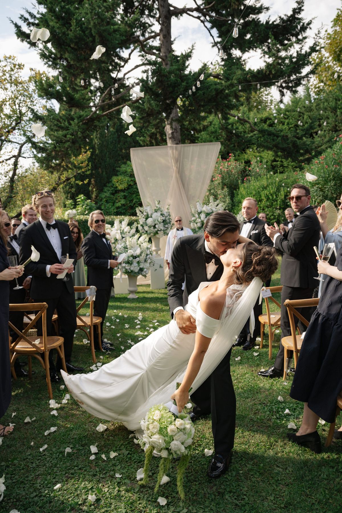 Groom dipping bride for a kiss as petals shower the ceremony aisle