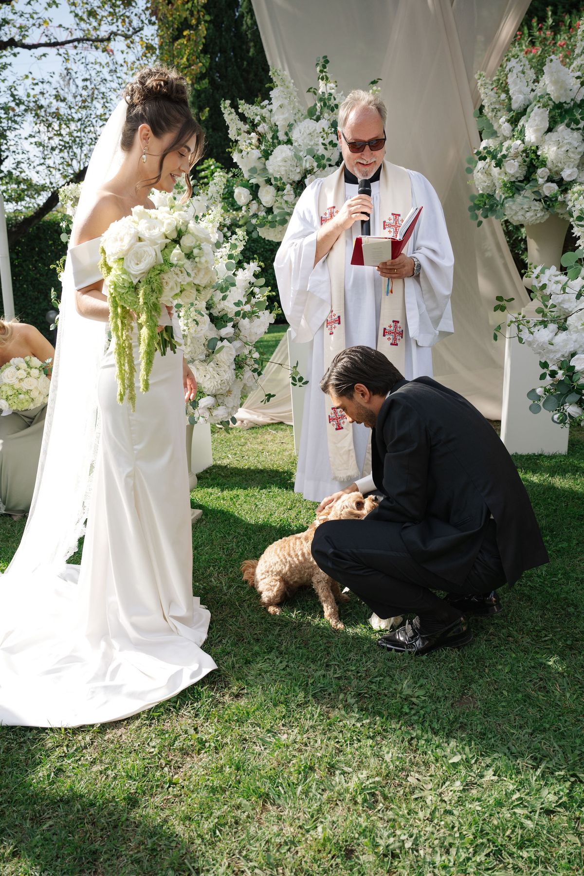 Groom kneeling to greet small dog at altar during outdoor ceremony