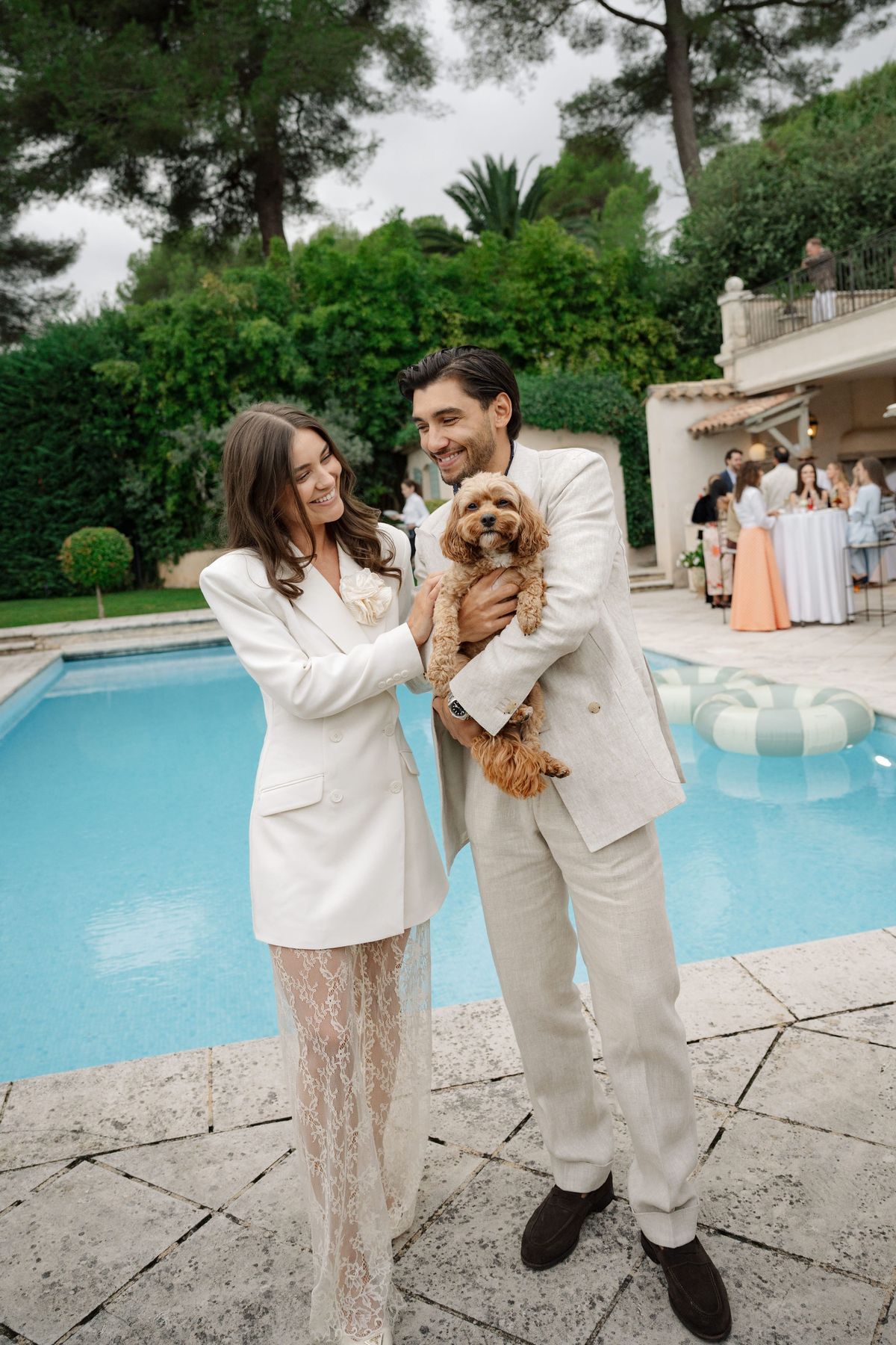 Couple in evening wear holding small dog beside pool at French venue