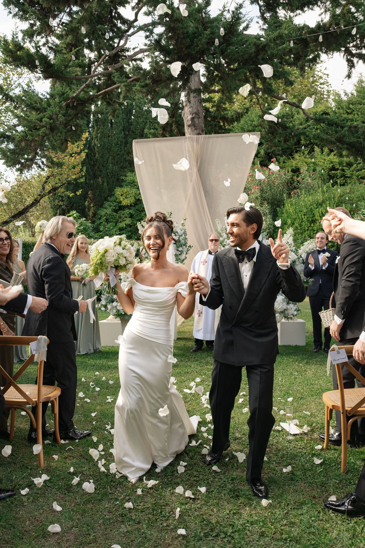 Newlywed couple walking up aisle through cheering shower of petals
