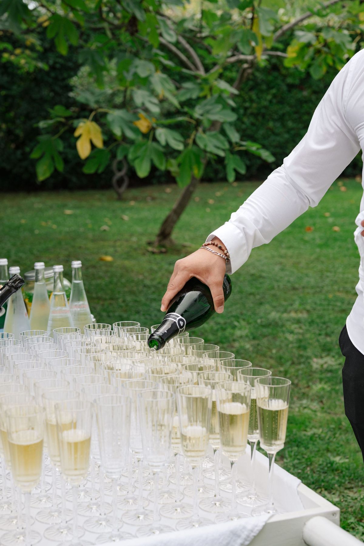 Waiter pouring champagne into rows of flutes on garden table