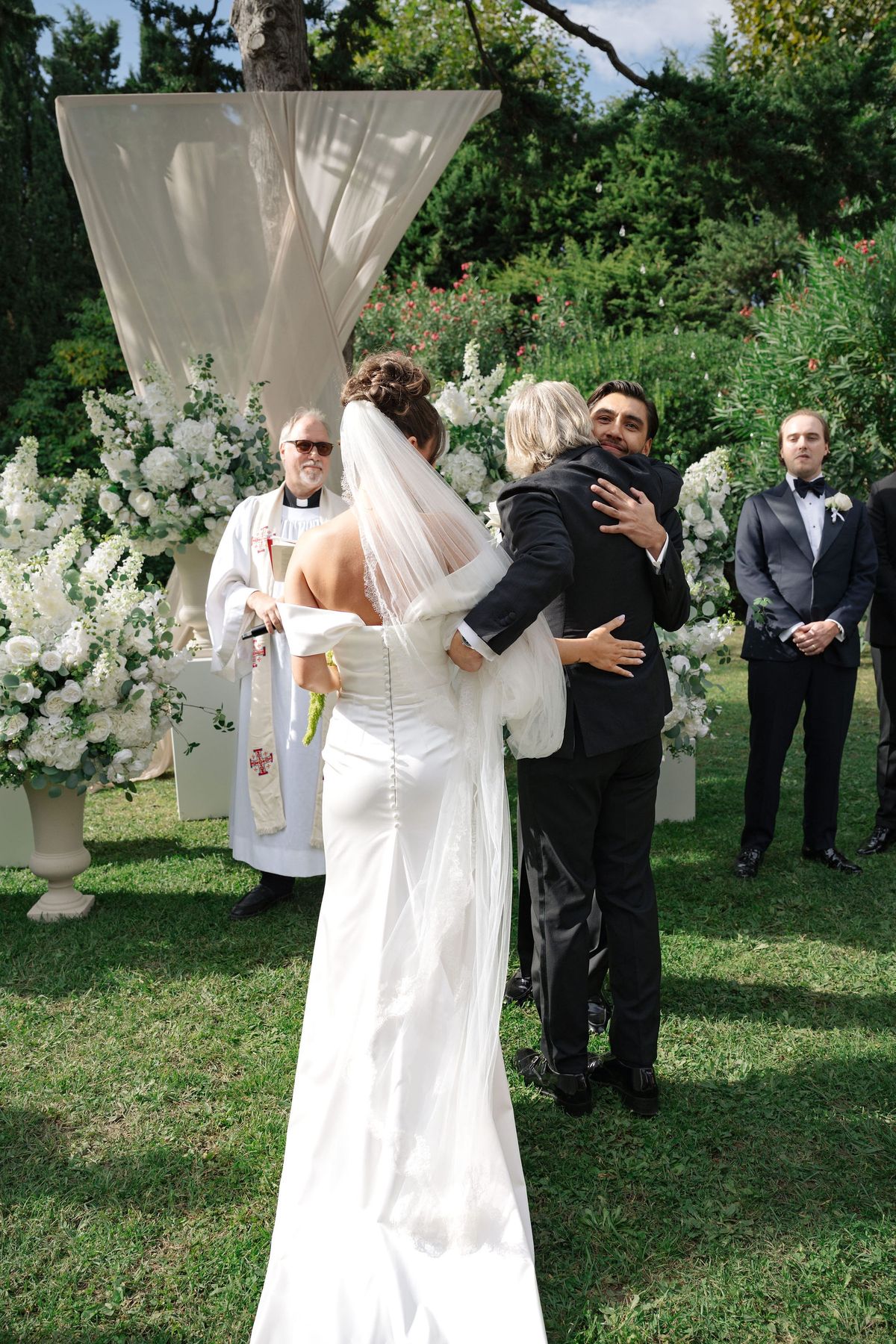 Groom hugging bride's parents at outdoor ceremony altar