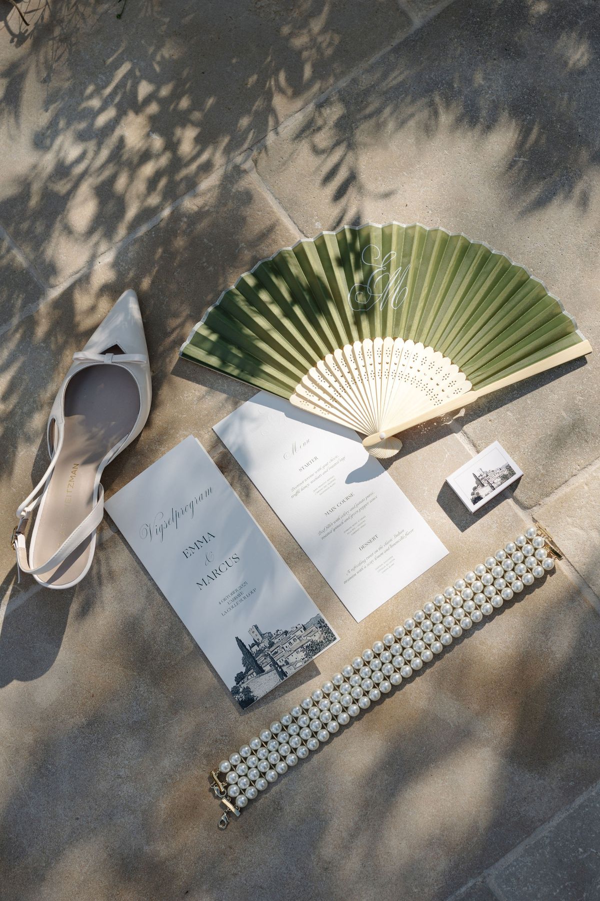 Flat lay of bridal shoe, sage fan, programme, and pearl bracelet