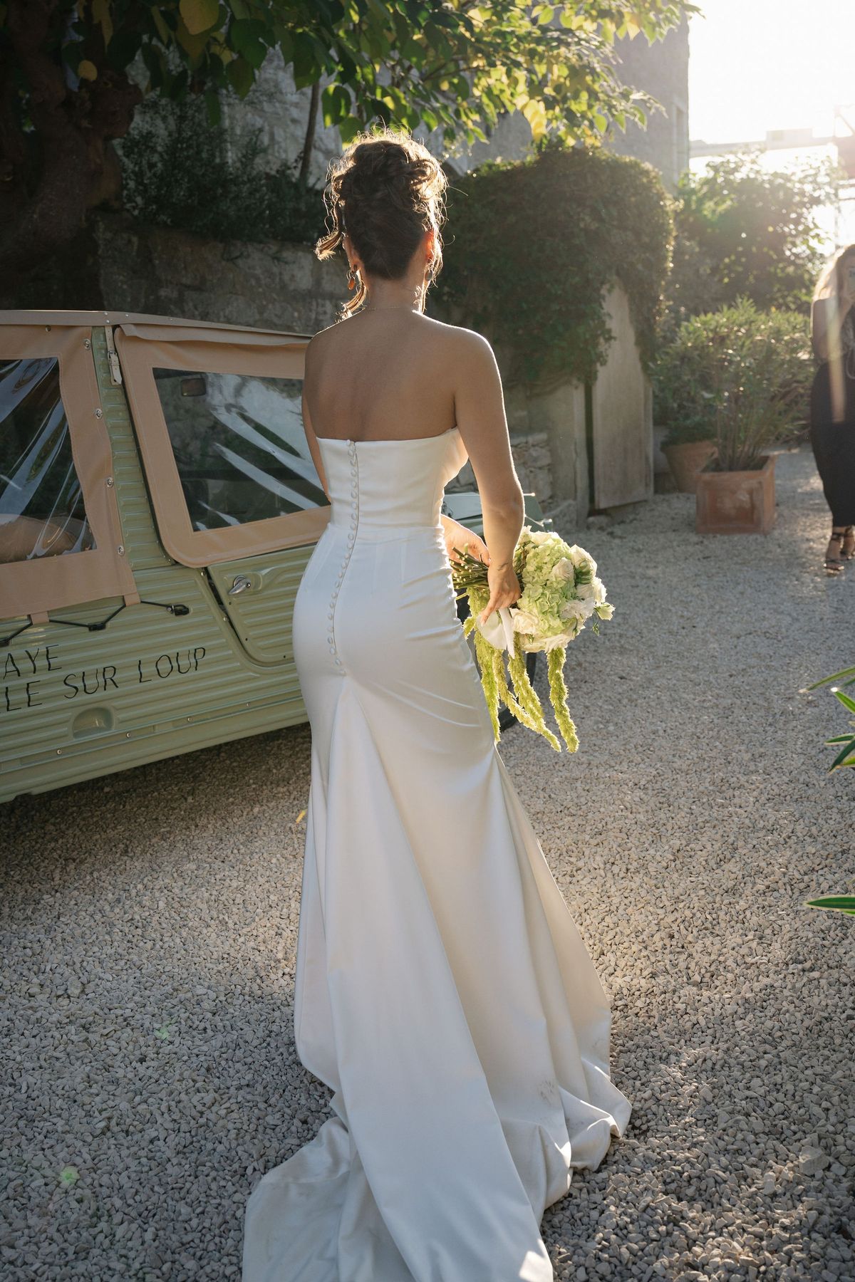 Bride walking toward vintage van at golden hour holding her bouquet