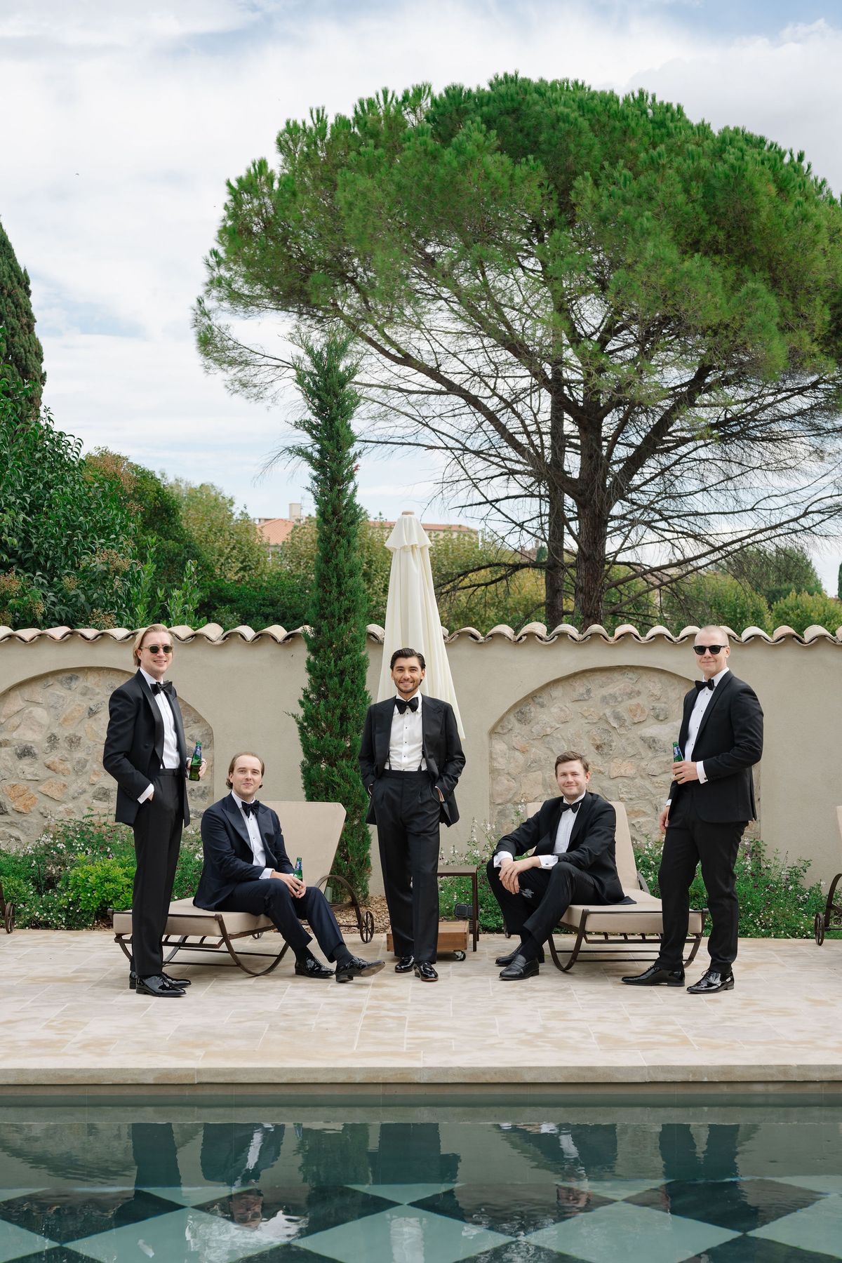 Groom and groomsmen in black tie posed beside checkerboard pool