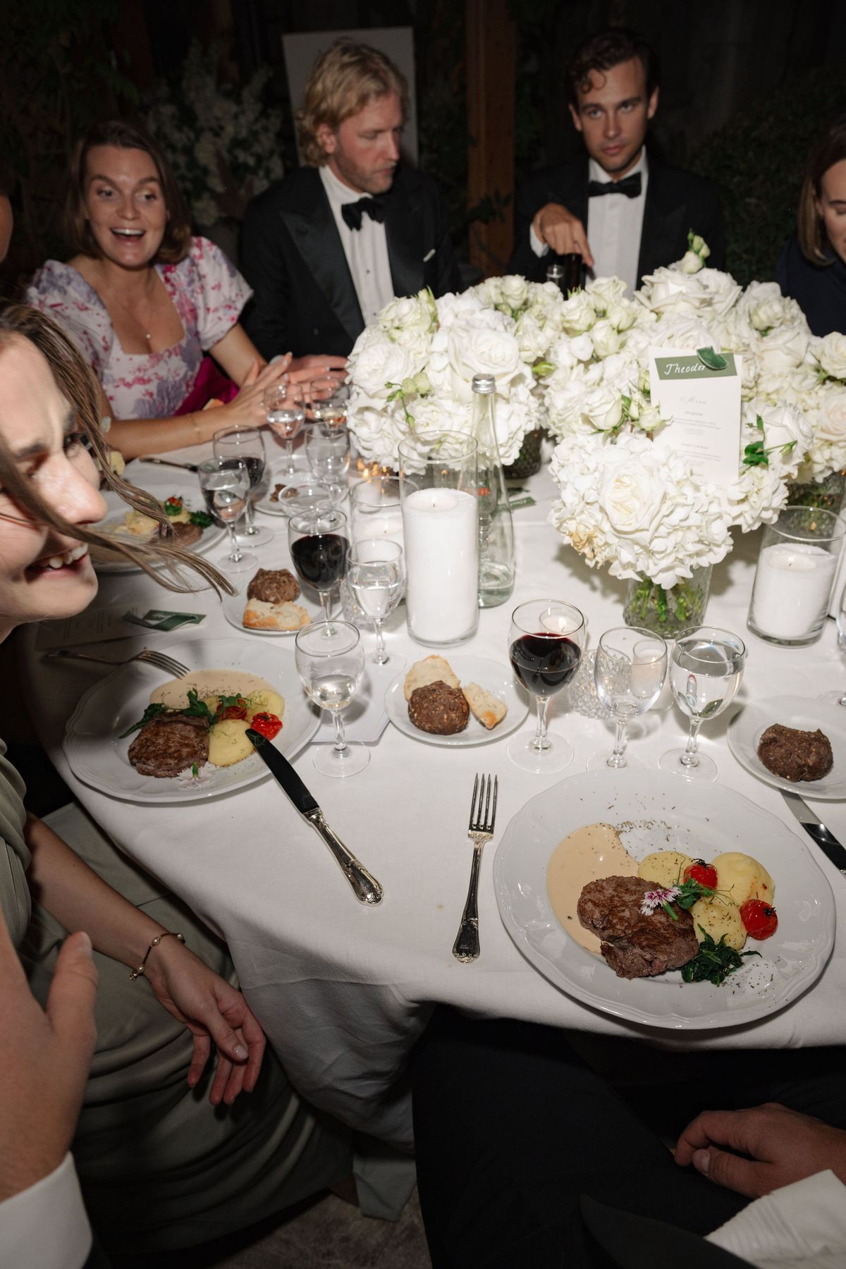 Guests dining at white floral round reception table with candles