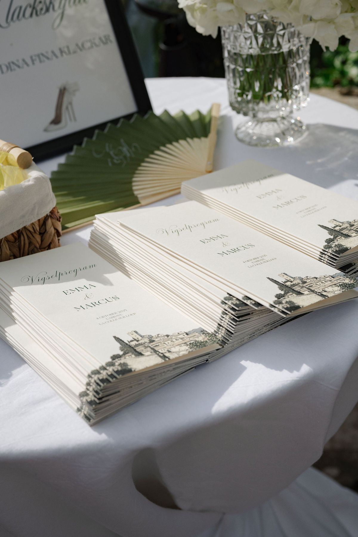 Stack of cream wedding programmes with sage fan and hydrangea on table