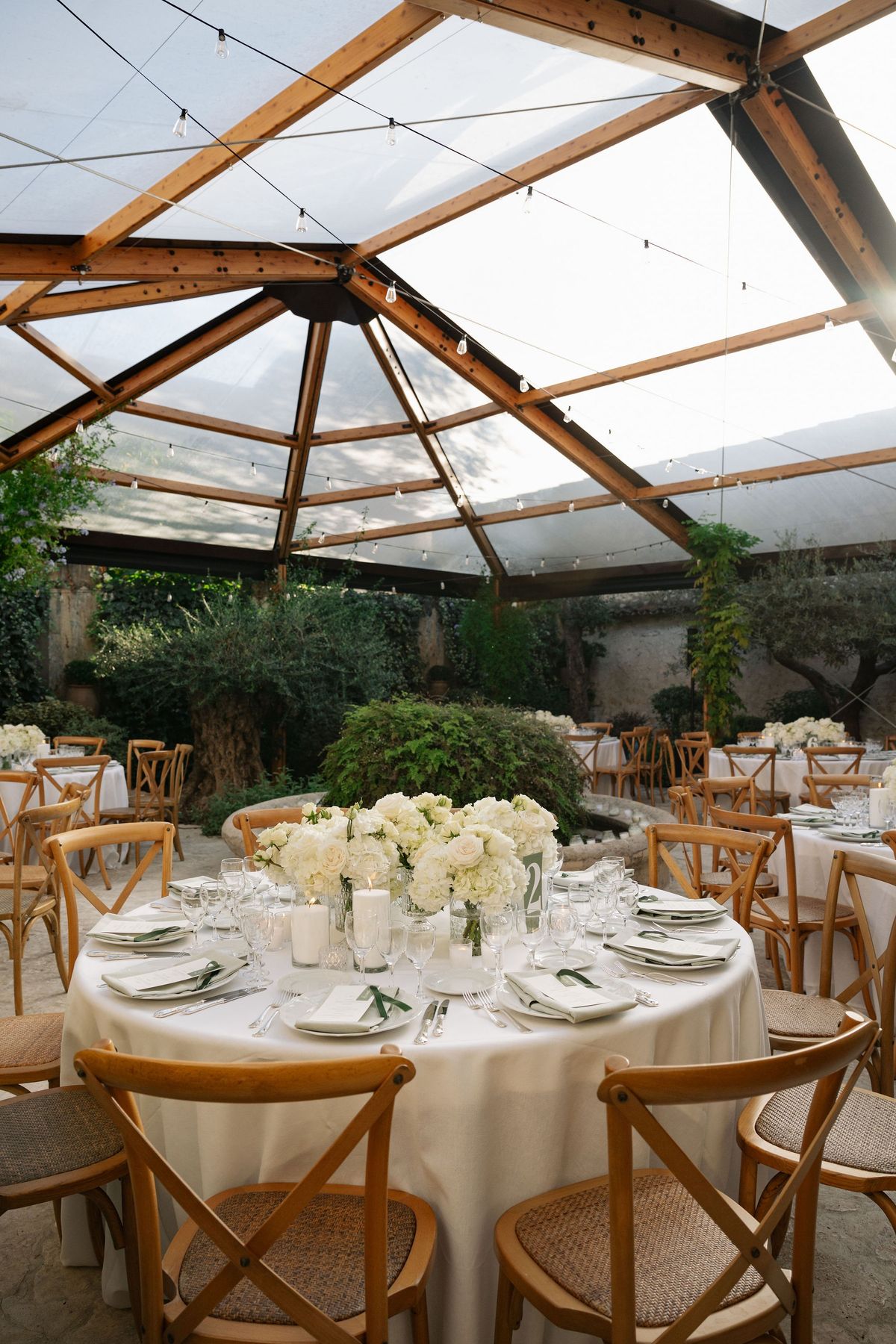 Glass marquee reception tables with white florals and crossback chairs