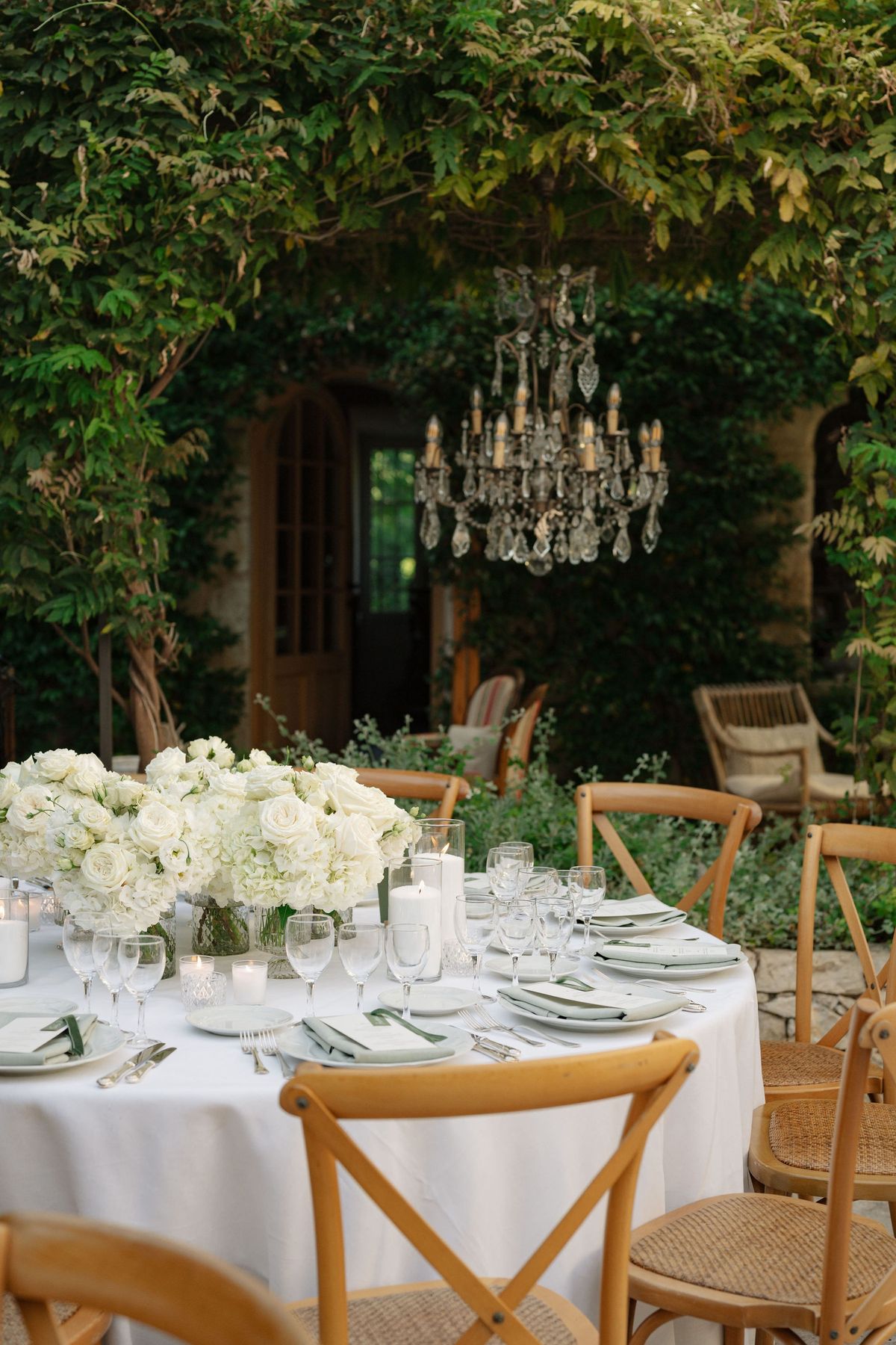 Crystal chandelier over white floral reception table in ivy courtyard