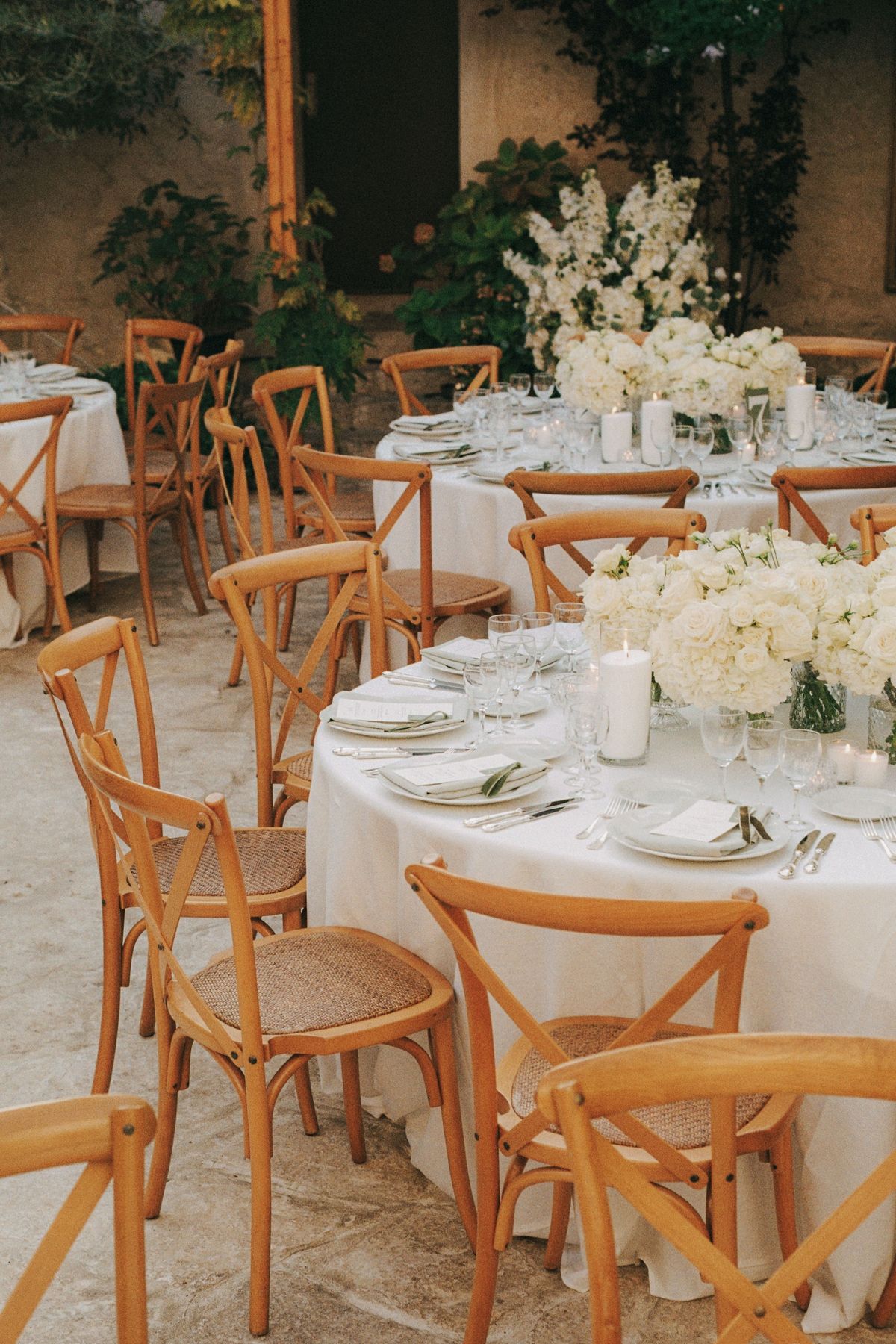 Two cream-linen reception tables with white florals and wooden chairs