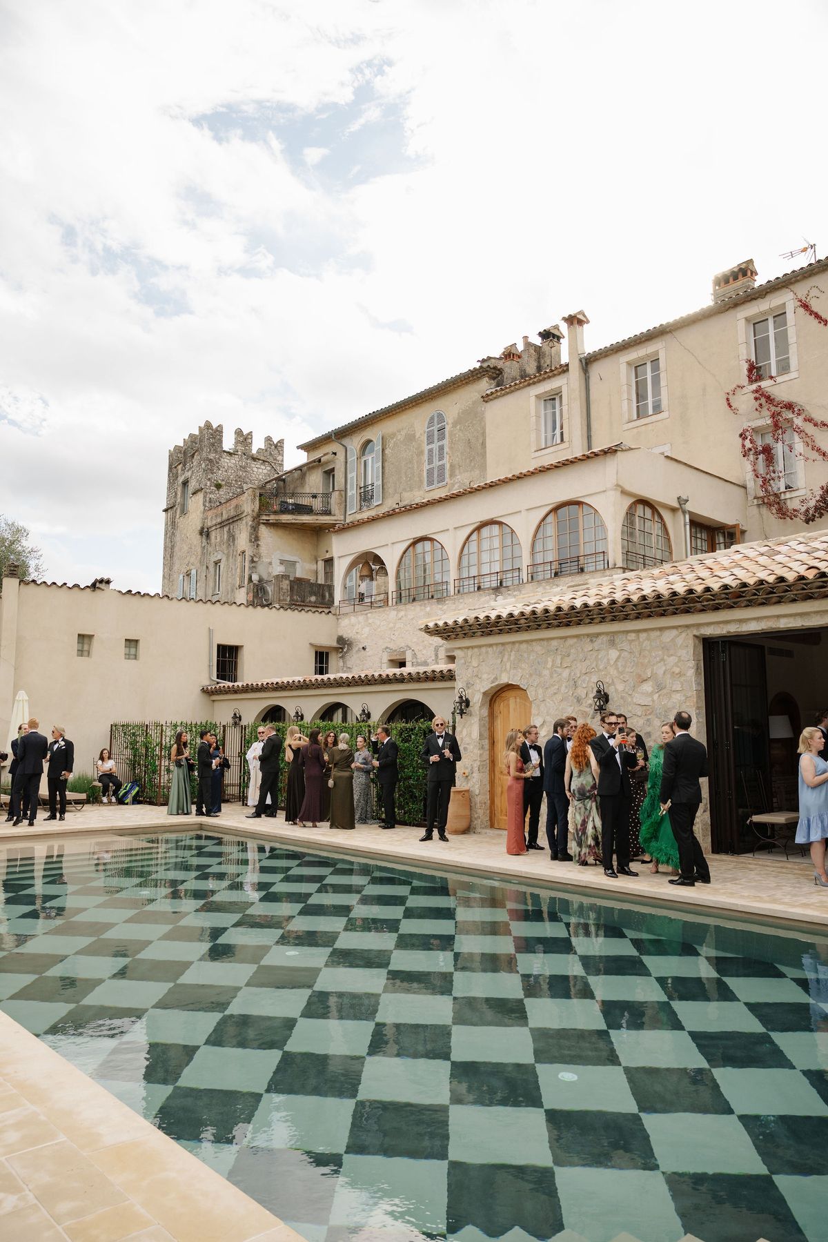 Guests at cocktail hour beside checkerboard pool and chateau bell tower