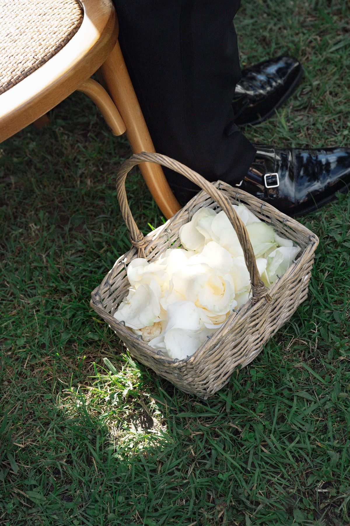 Wicker basket of white rose petals tucked beneath ceremony chair