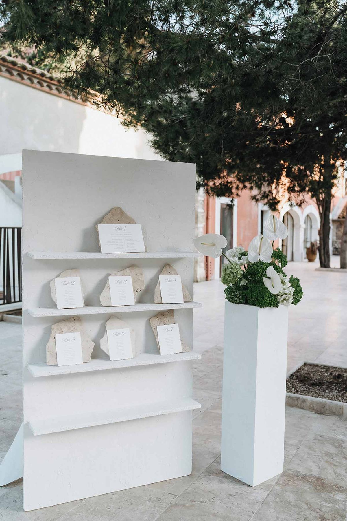 Seating chart display on white plaster shelves with limestone card holders and white anthurium arrangement