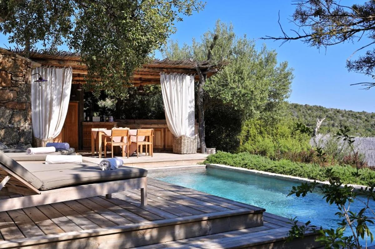 Private pool area with wooden deck, sun loungers, and white linen cabana pergola at stone property