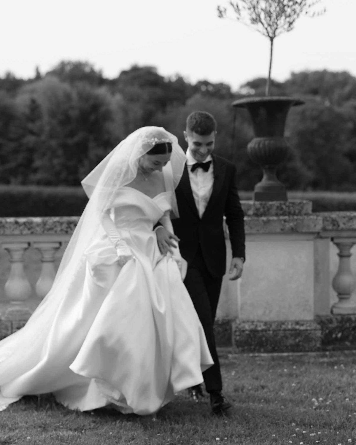 Bride and groom walking and smiling on chateau grounds with stone balustrade in black and white