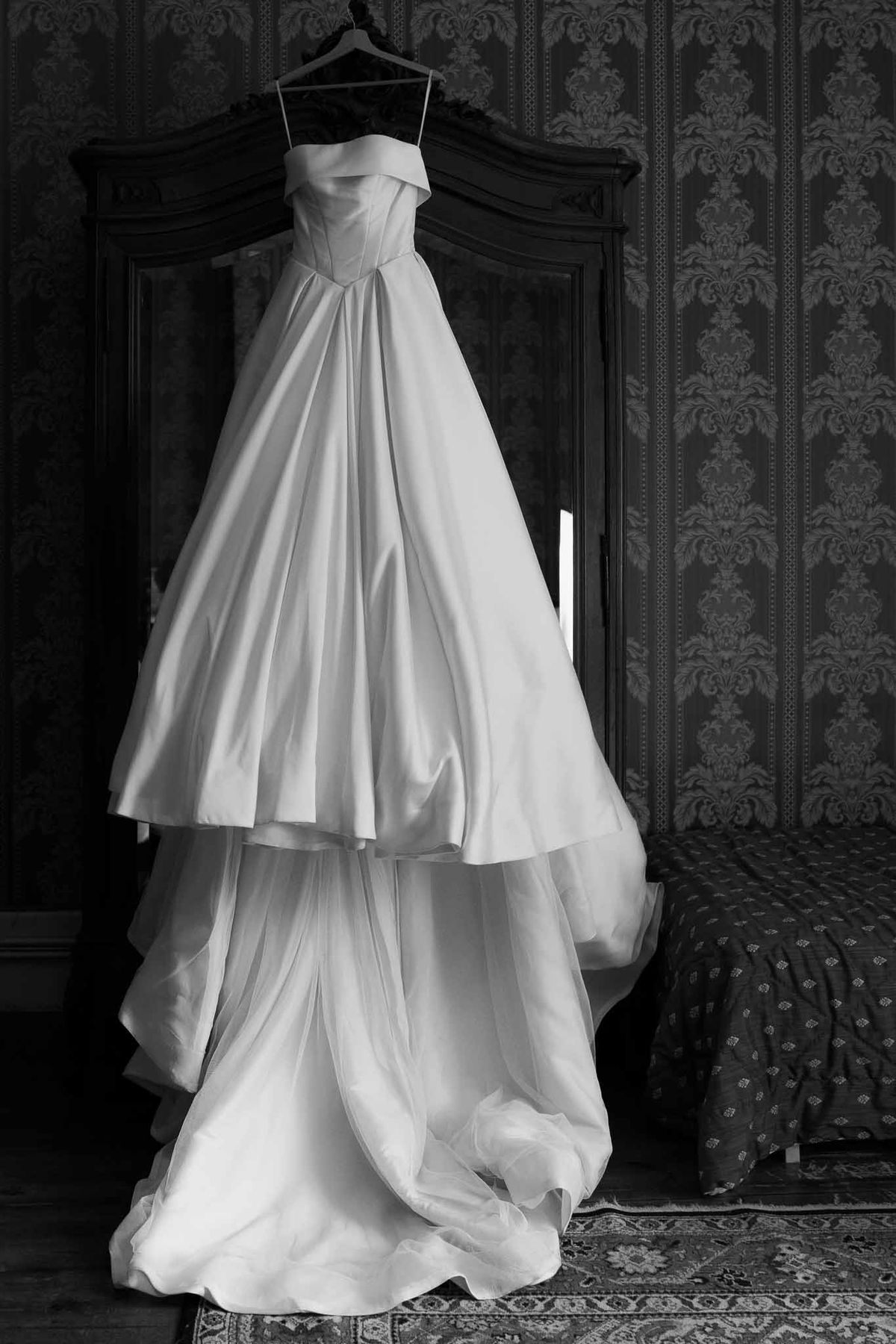 Black and white strapless ballgown with tiered skirt hanging from wooden armoire in damask room
