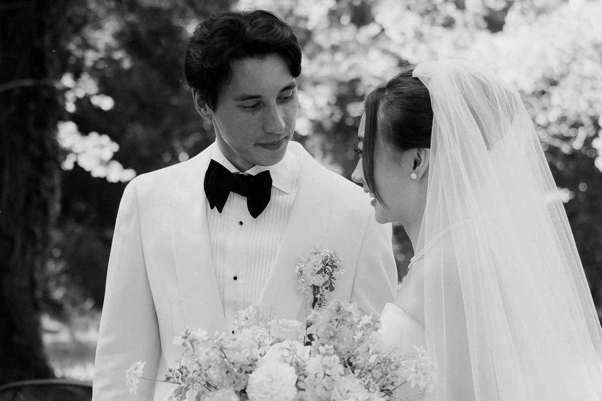 Black and white close-up couple facing each other bride with veil and peony bouquet groom in white dinner jacket