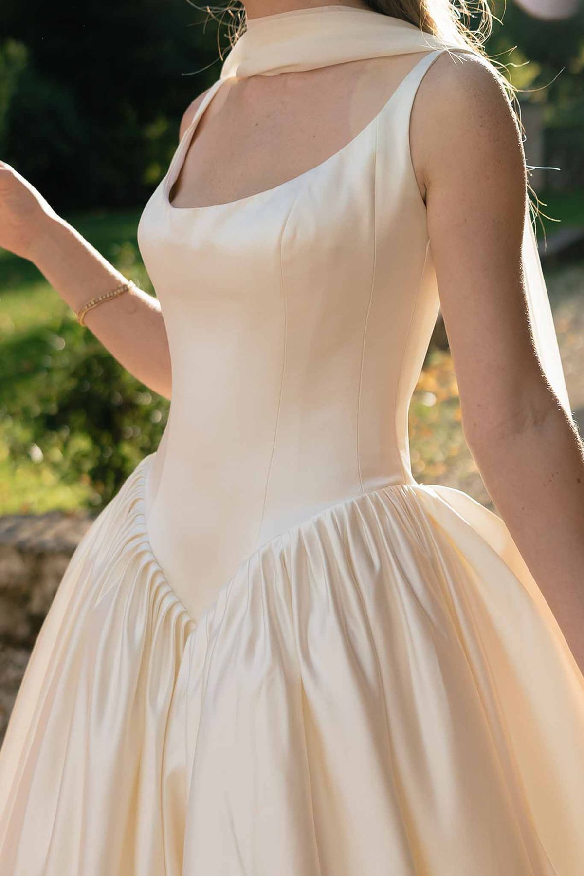 Close-up of ivory satin corset bodice ball gown with gathered skirt and draped veil in golden light