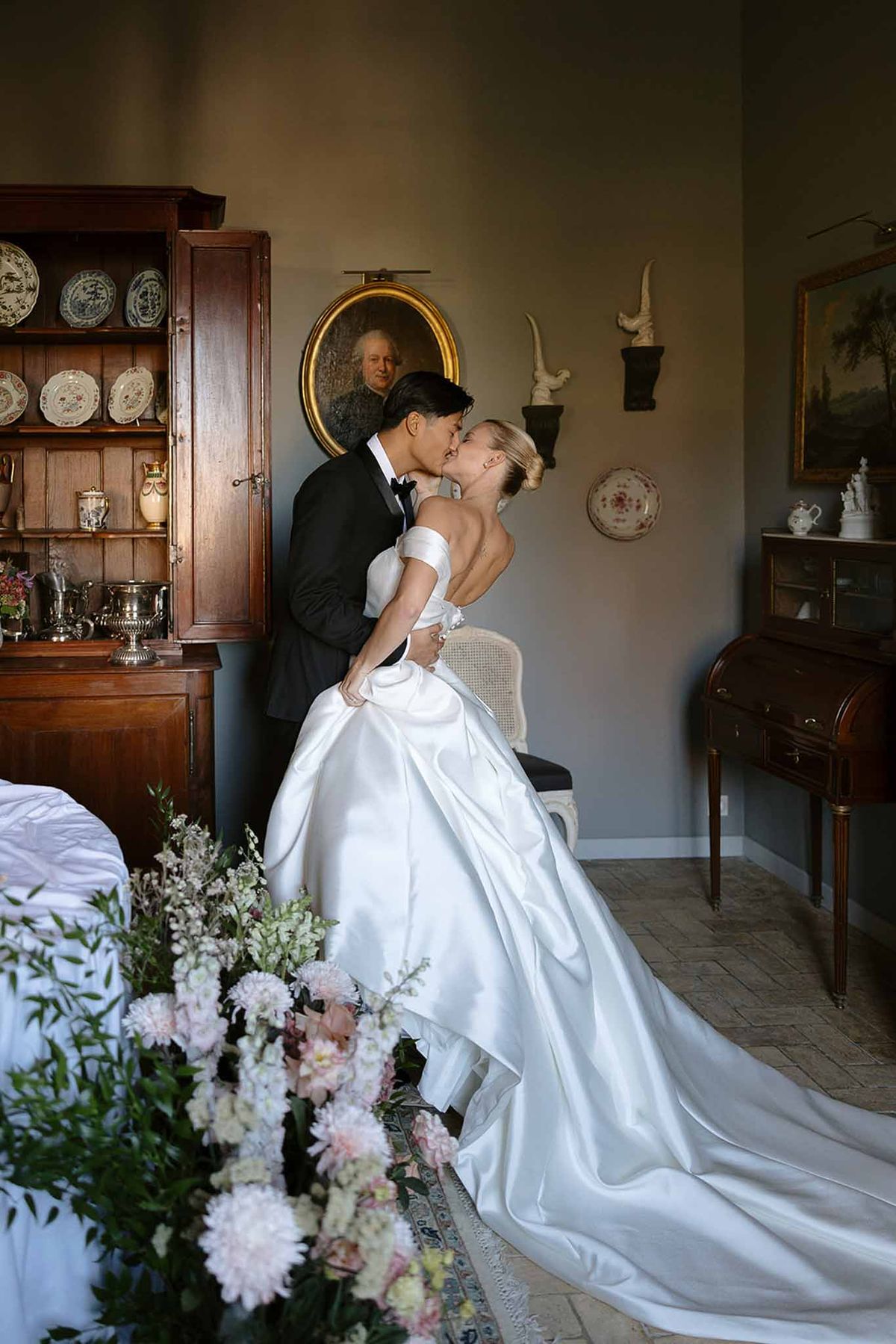 Couple kissing in antique chateau room with blue walls, oil paintings, and dahlia arrangement