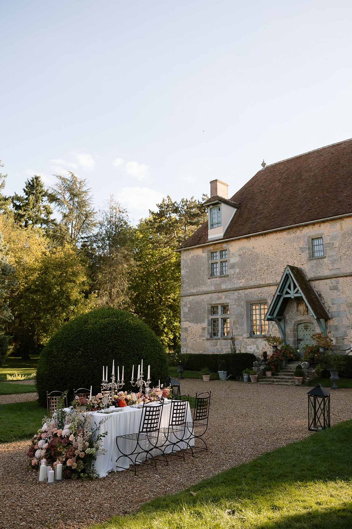 Long table with silver candelabras and cascading blush dahlia arrangements before stone manor with terracotta roof