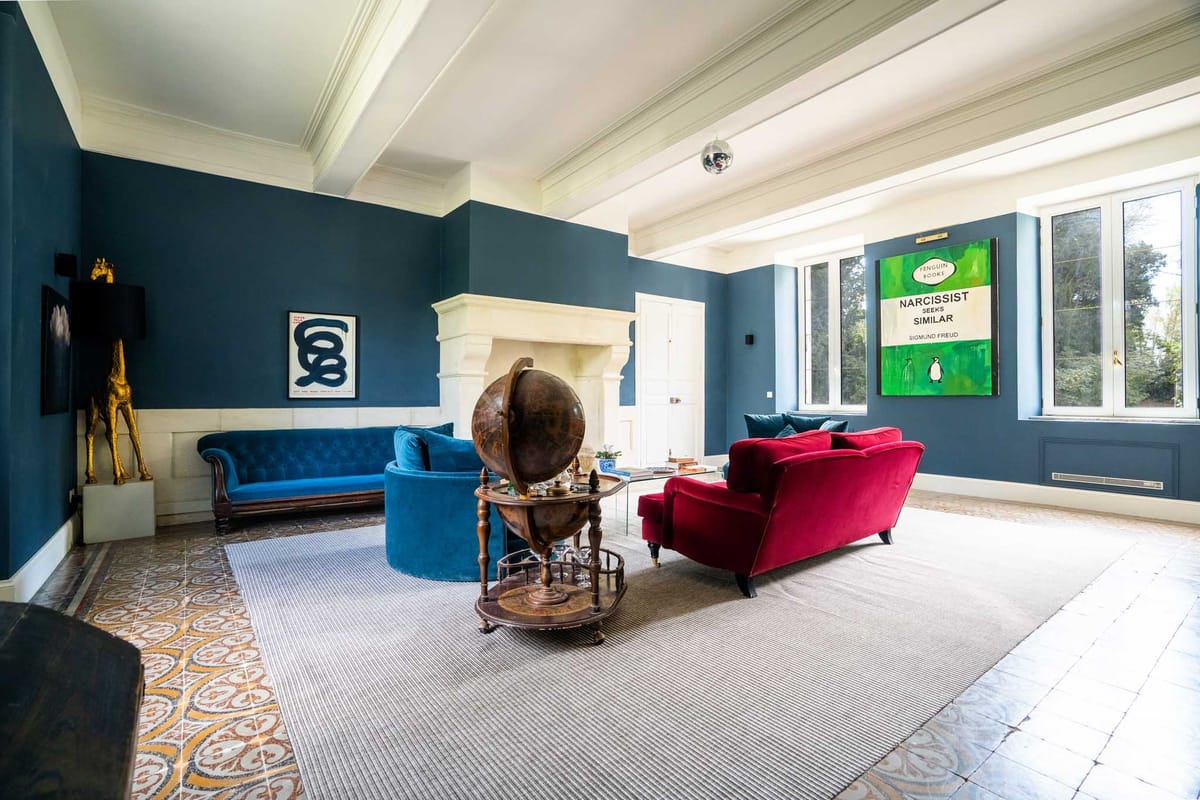Eclectic lounge with navy walls, teal and crimson velvet sofas, gold giraffe sculpture, and pop art prints