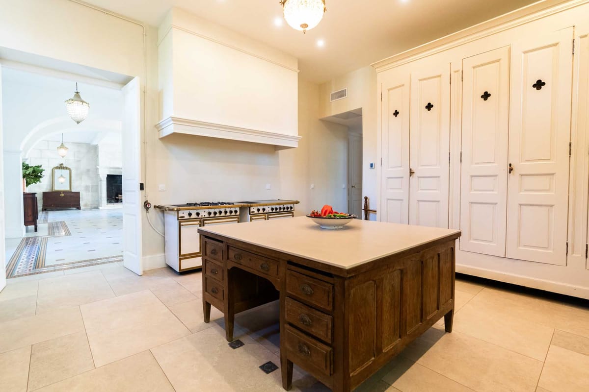 Chateau kitchen with antique wood island, brass range cooker, and adjacent room with fireplace