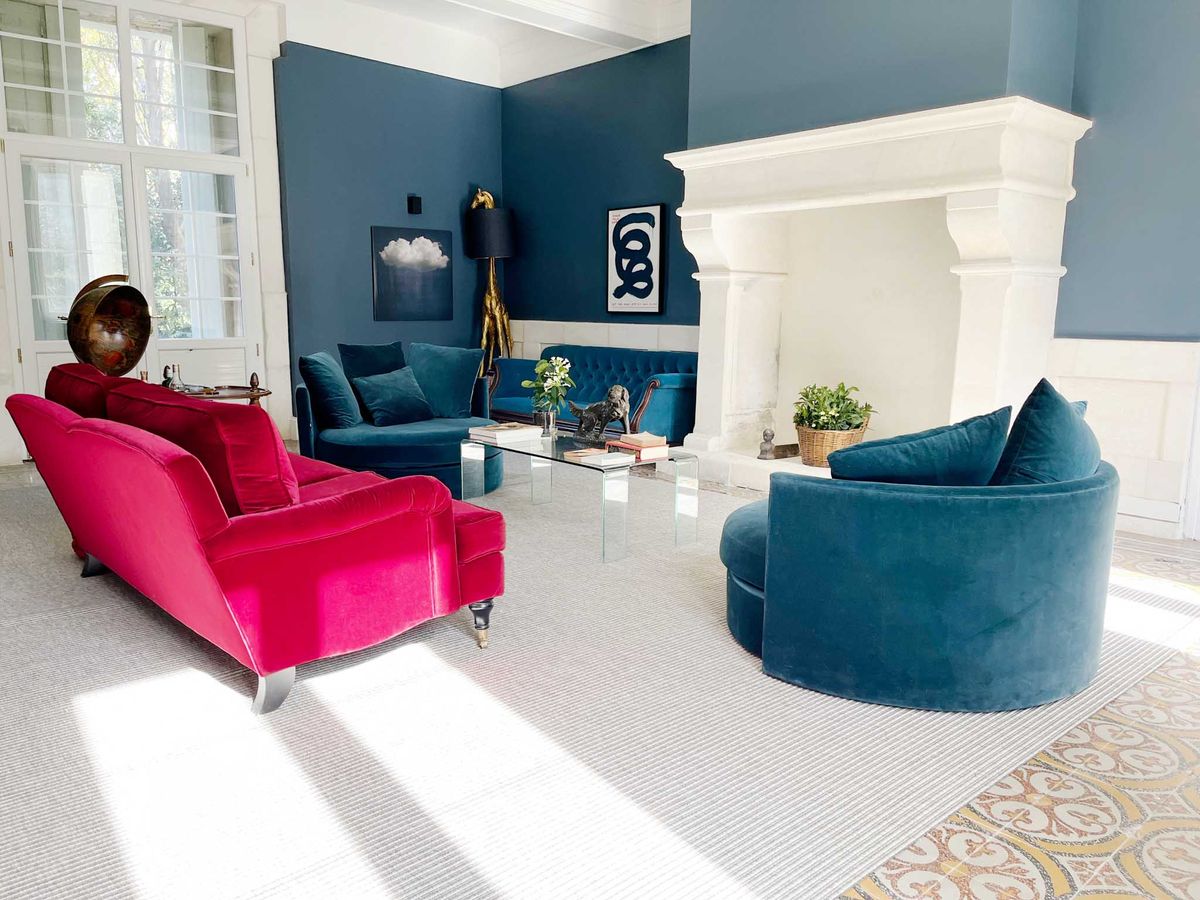 Interior salon of French chateau with teal walls, fuchsia velvet sofa, chesterfield seating, and patterned tile floors