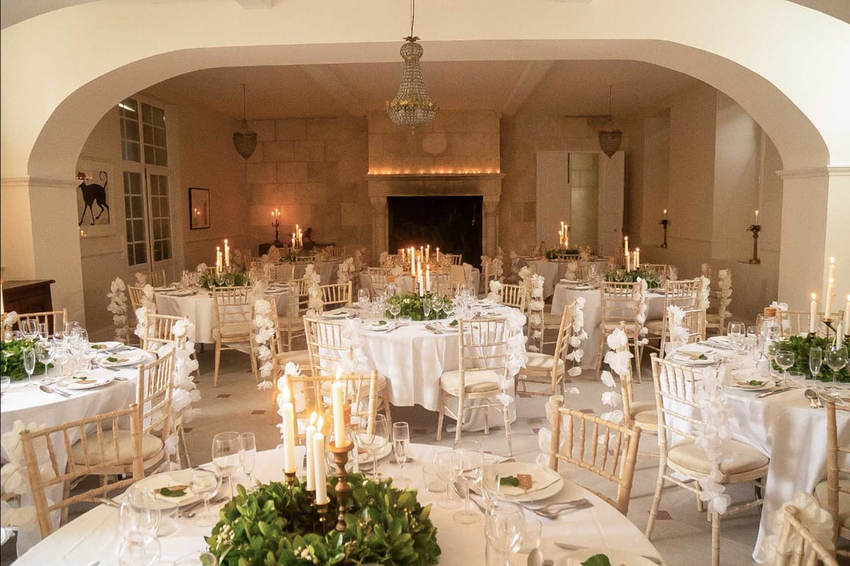 Chateau dining room with round tables, white orchid chair decor, brass candelabras, stone fireplace and chandelier