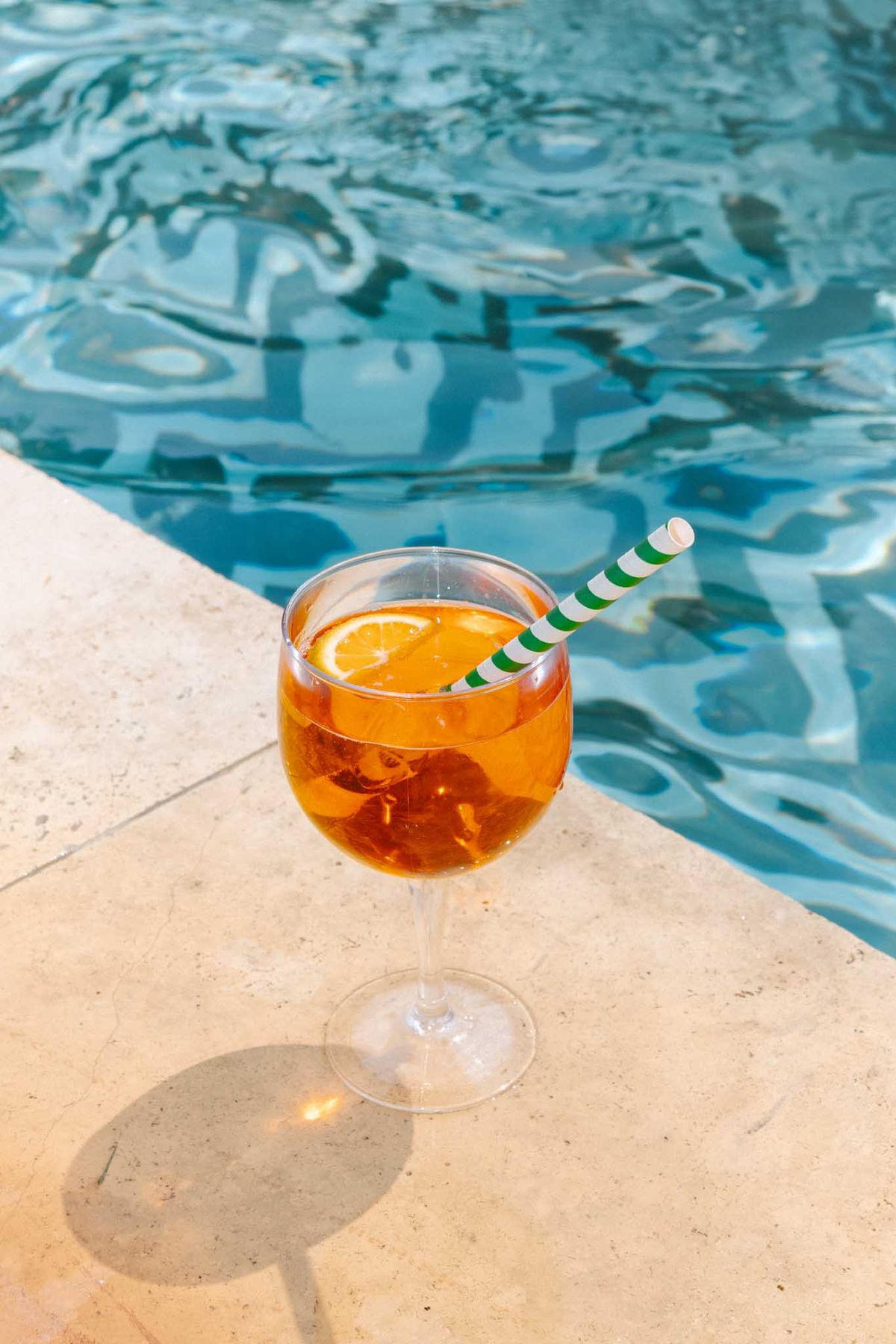 Aperol Spritz cocktail with orange garnish on poolside stone edge in bright sunlight