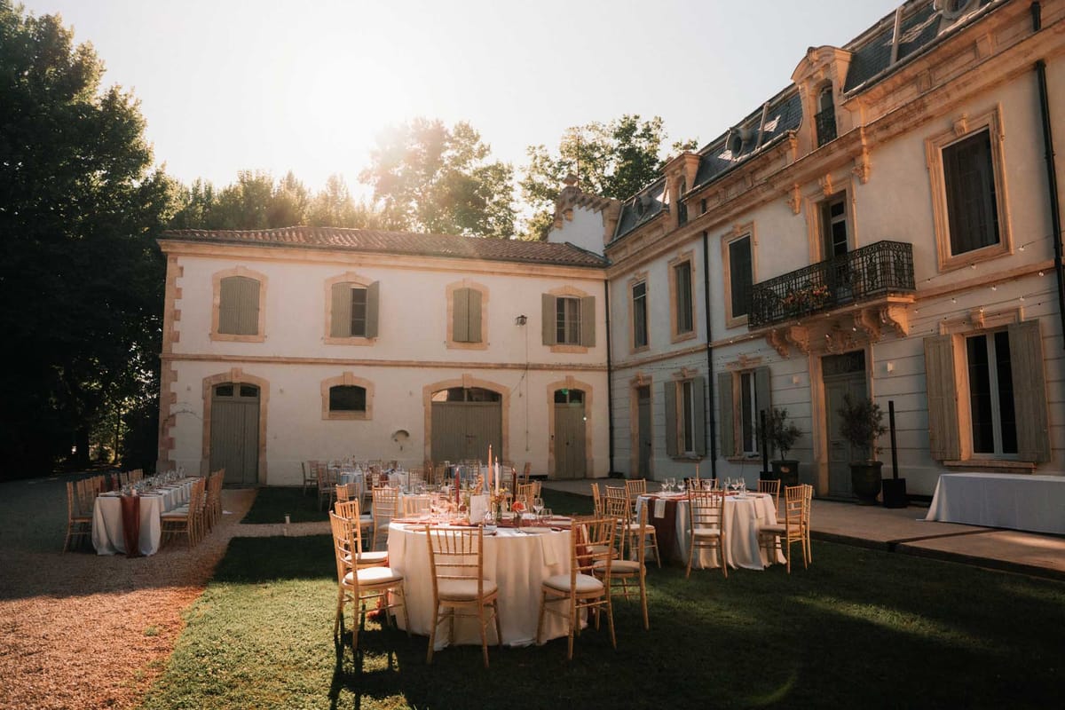 Outdoor chateau courtyard reception setup with round and rectangular tables, gold Chiavari chairs, and terracotta candles