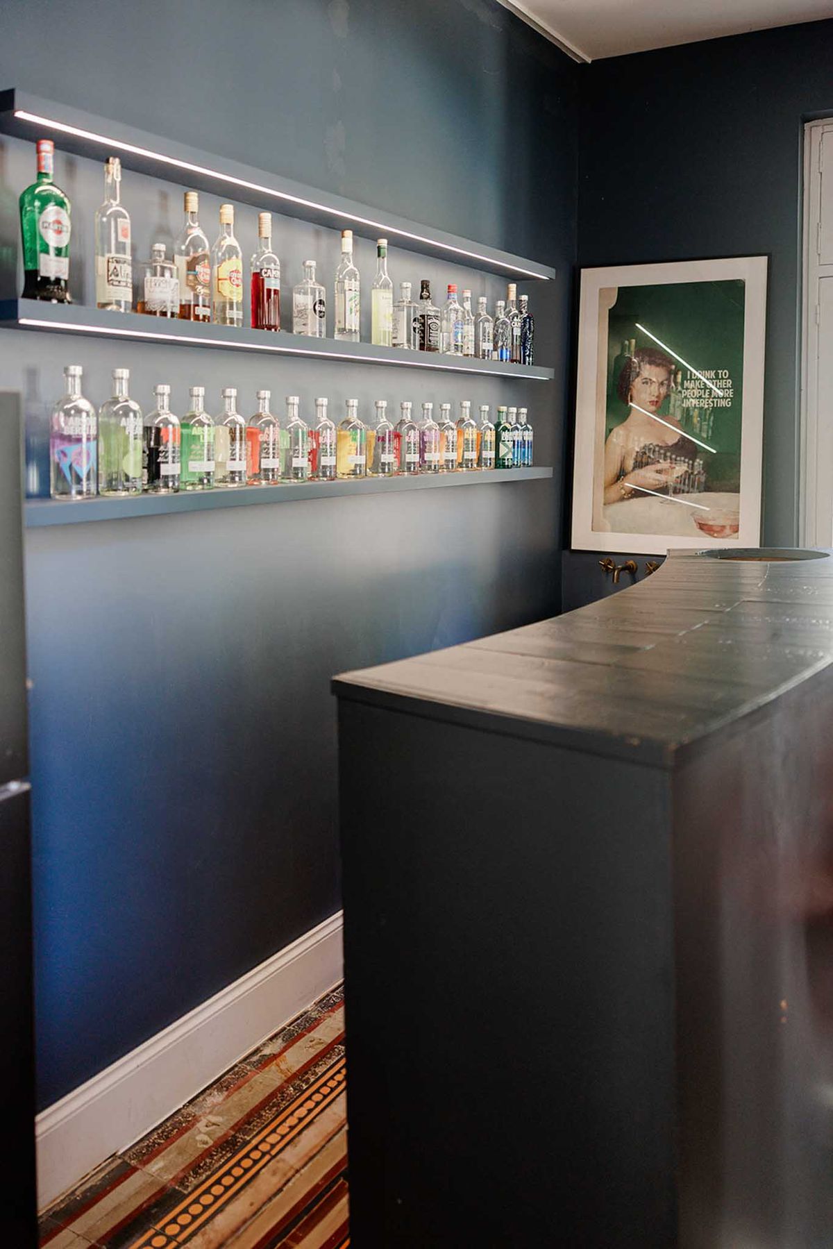 Navy blue bar room with illuminated spirit shelves, encaustic tile floor, and retro wall print