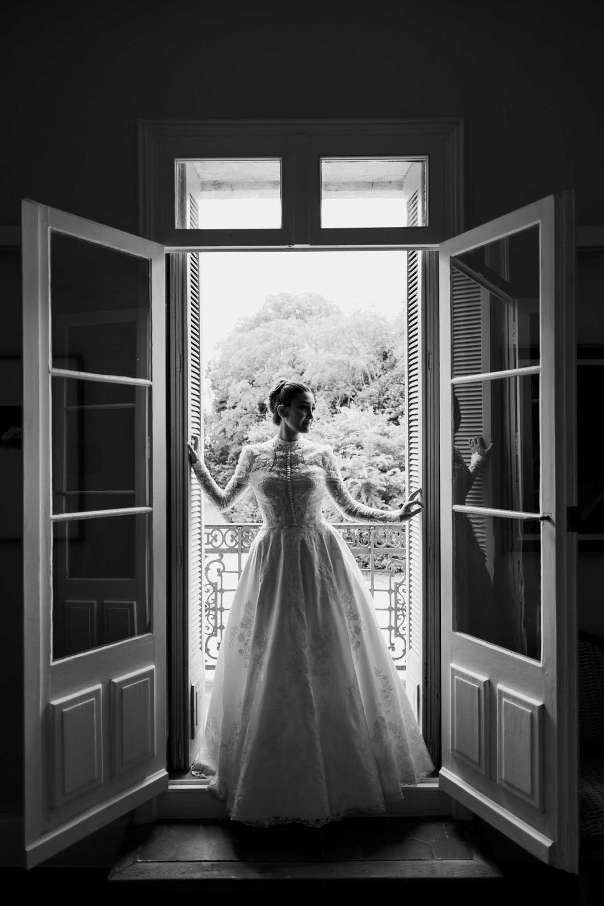 Black-and-white backlit bridal portrait in open French doors with lace ball gown and long sleeves