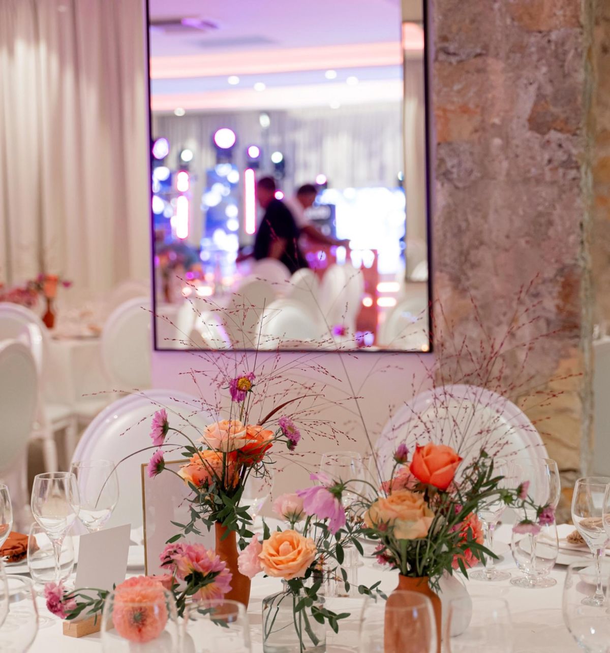 Reception table with peach roses, coral ranunculus, and rust napkins in terracotta vases at stone-walled venue