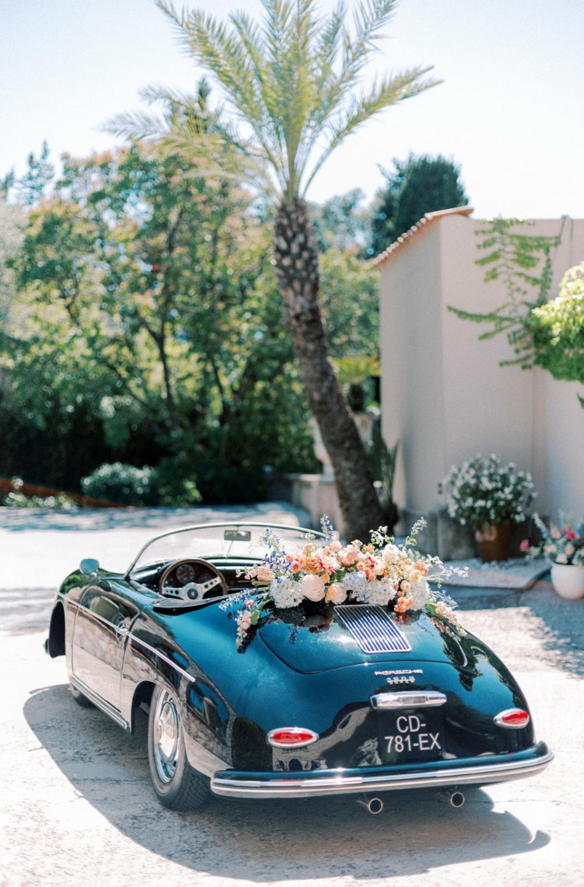 Black vintage Porsche 356 convertible decorated with peach roses and cream hydrangeas in sunlit courtyard