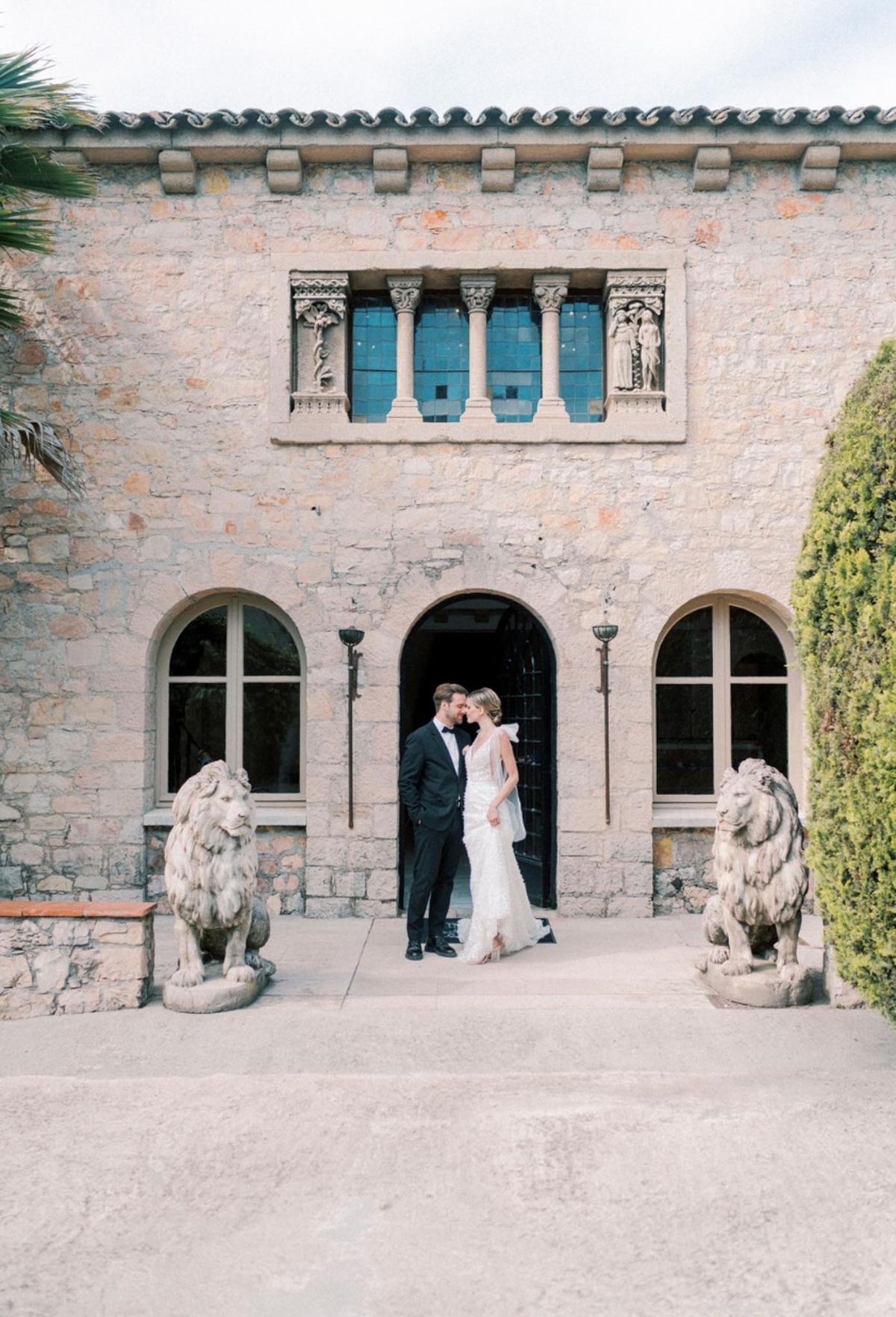 Couple touching foreheads under Romanesque stone archway flanked by lion statues at French Riviera venue