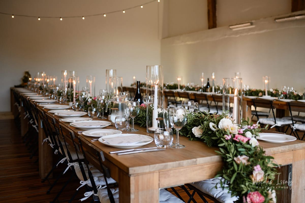 Barn reception with farm tables, green garlands, cream peonies, and globe string lights