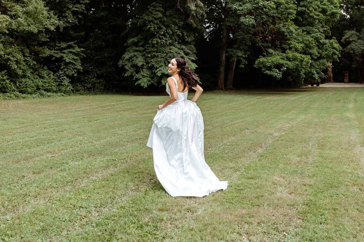 Bride mid-turn on parkland lawn with corseted satin ballgown train lifted in motion