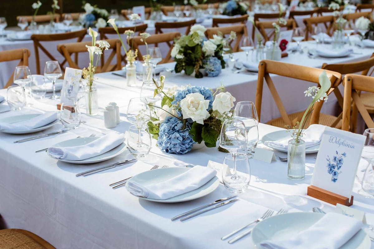 Blue hydrangea and ivory rose centrepieces with calla lily bud vases on white linen banquet tables