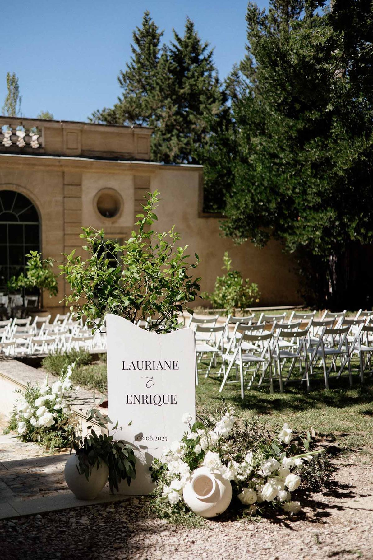 White welcome sign with rose urns before ceremony chairs on lawn at ochre stone chateau