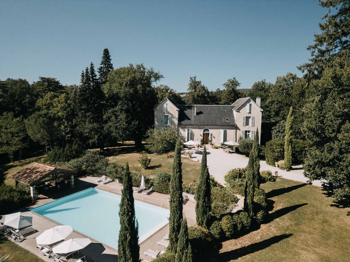 Aerial view of stone manor with slate roof, cypress-lined drive, rectangular pool, and timber pool house