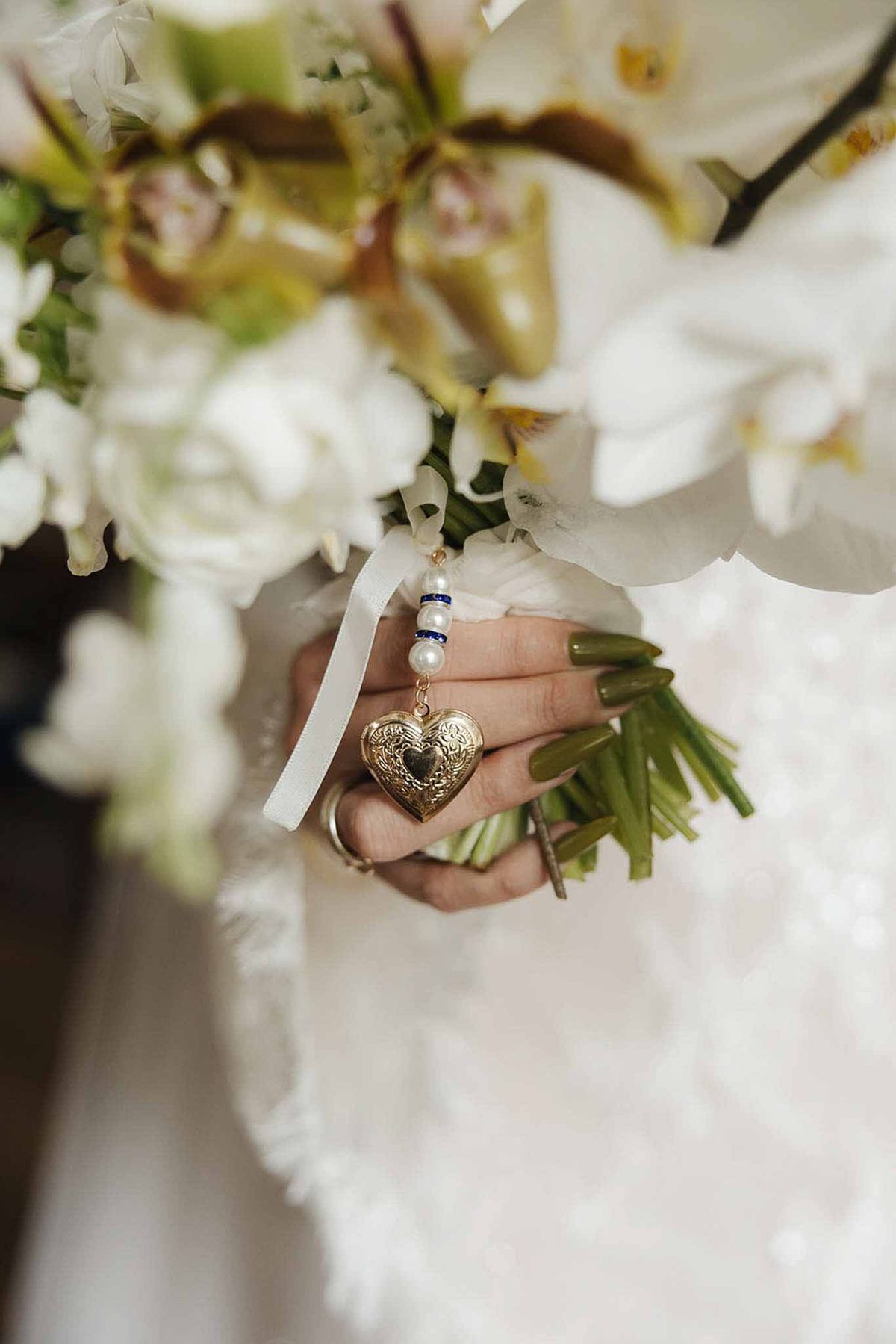 Close-up of white orchid bouquet with gold heart locket charm on pearl and blue beaded strand in bride's hand