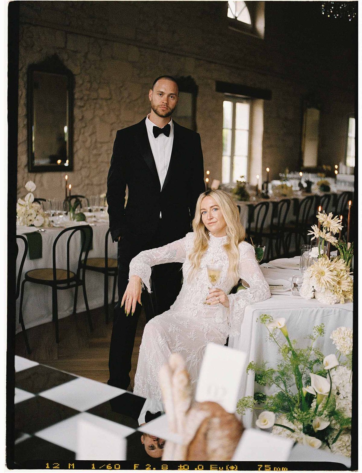 Bride and groom at reception head table in stone-walled chateau with checkered floor and taper candles