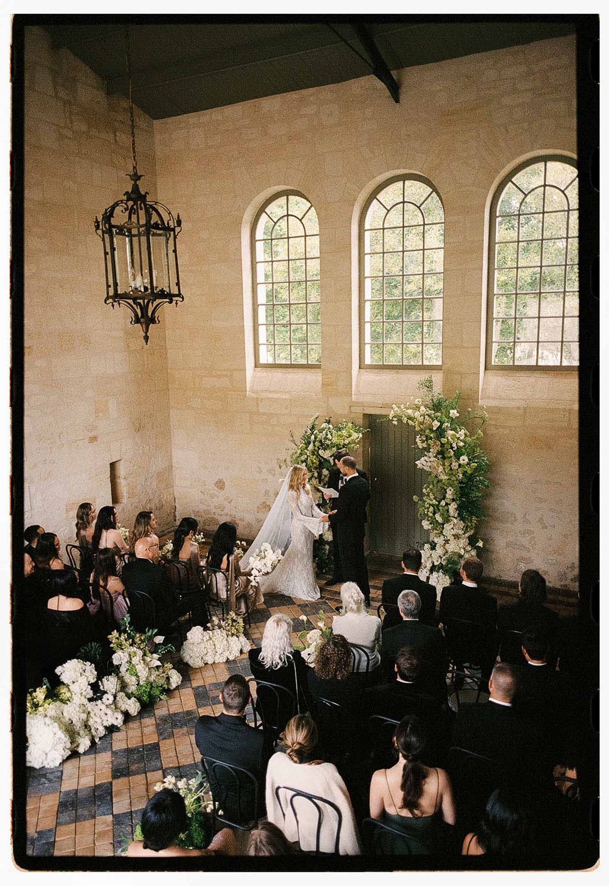 Indoor ceremony in historic chapel with white hydrangea arch, checkered floor, and 40 seated guests