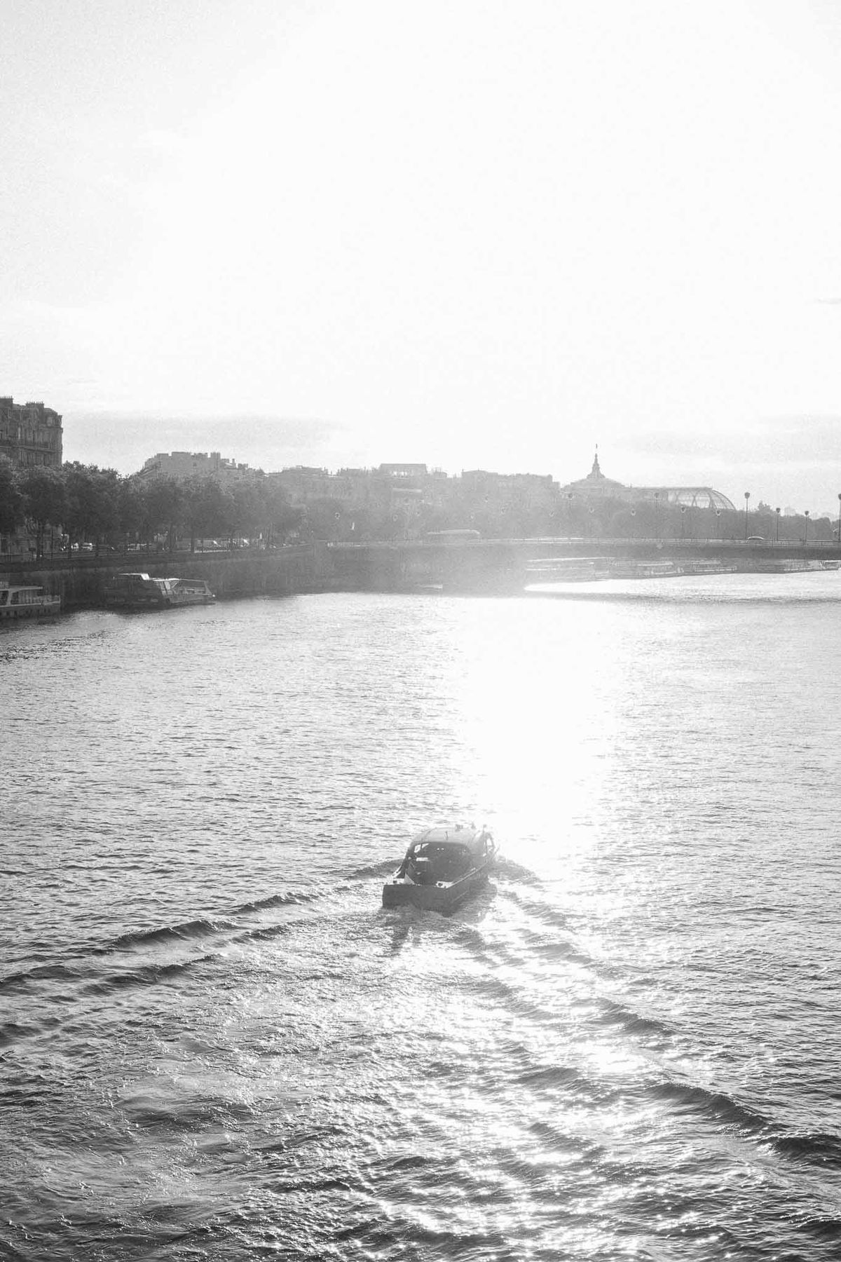 Black and white Seine River scene with motorboat wake and Haussmann buildings on distant bank
