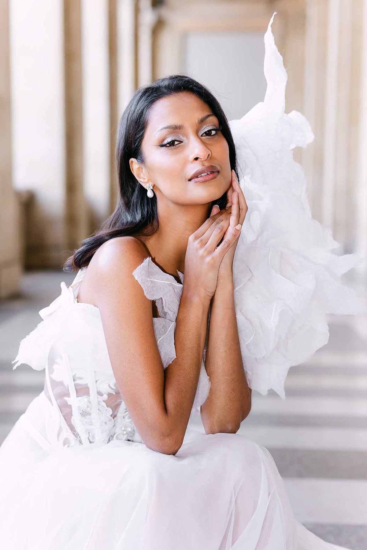 Bride in strapless white lace corset gown with organza ruffle details seated in classical stone arcade