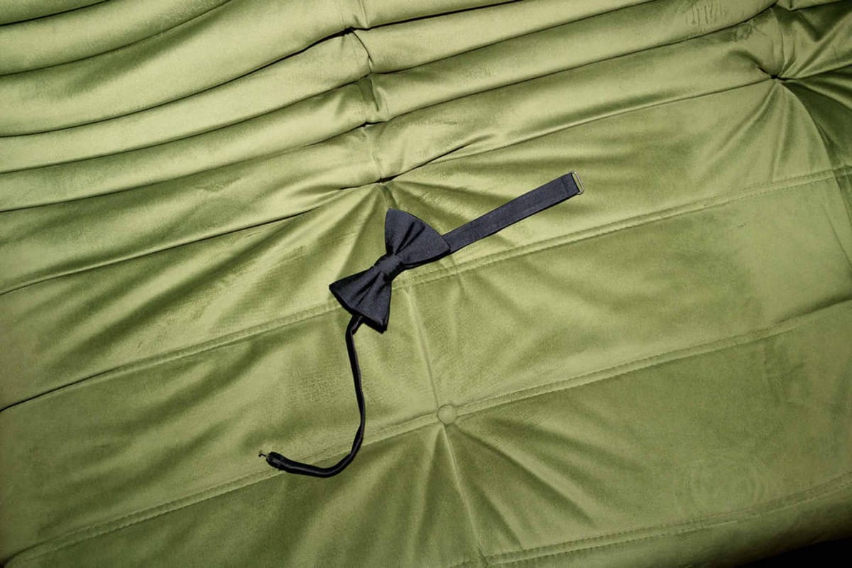Navy bow tie resting on olive green tufted velvet surface during groom preparations