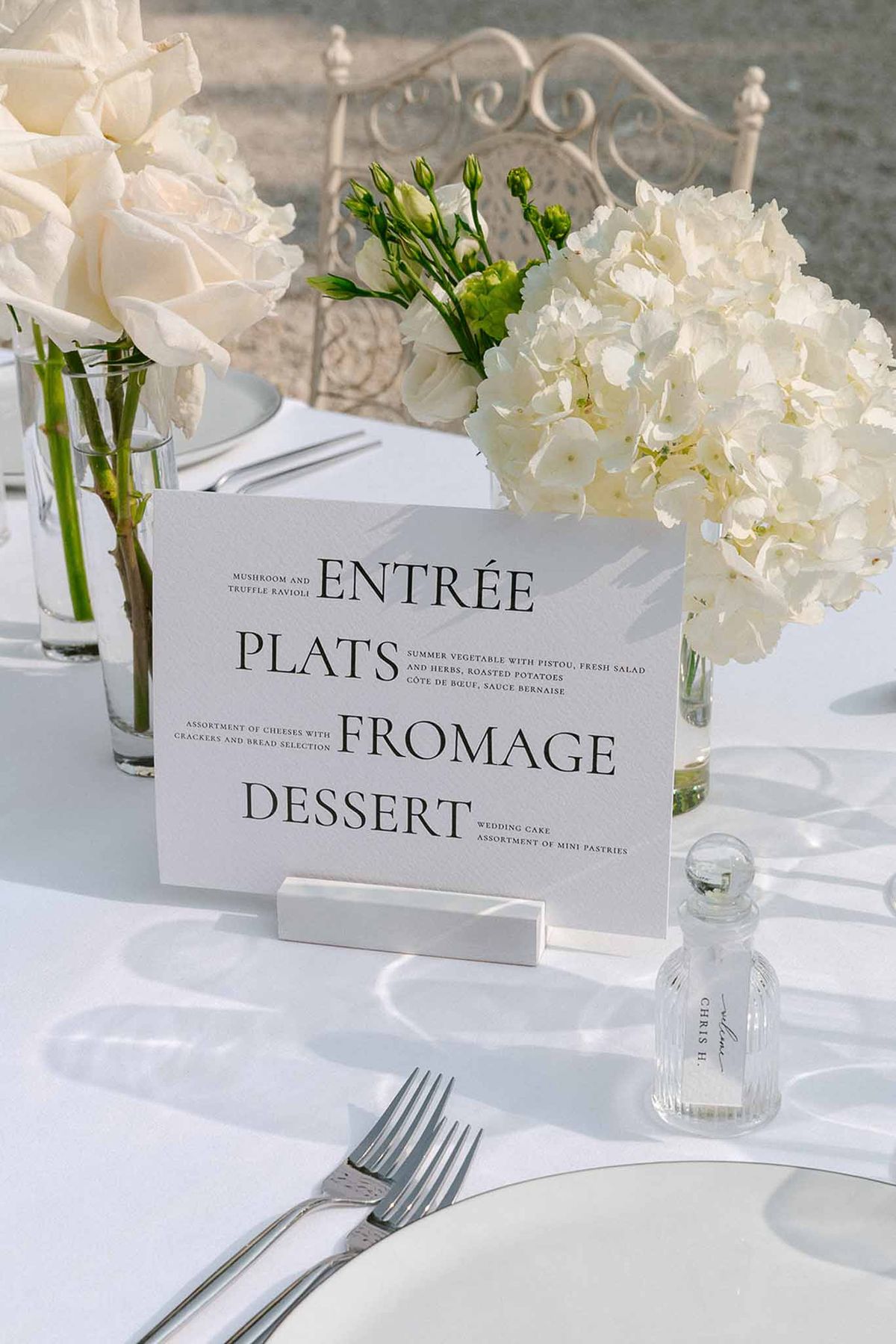 Printed French-English menu card in marble holder on white-dressed reception table with ivory hydrangea arrangements